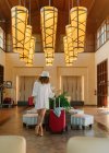 Mulher irreconhecível em roupas brancas casuais com mala vermelha esperando pelo lobby do hotel — Fotografia de Stock