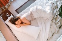 Von oben ruhig schlafende Frau in weißem Bett neben Nachttisch mit runder Tasse Kaffee und Smartphone am Morgen — Stockfoto
