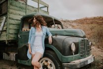 Молодая женщина в шортах и джинсовой рубашке стоит у зеленого грузовика и смотрит вдаль на природу — стоковое фото