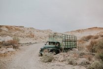 Песчаные холмы и грязная дорога с винтажным грузовиком, припаркованным на обочине дороги сухими кустами днем — стоковое фото