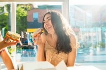 Щасливі жінки їдять глазуровані десерти, сидячи за столом біля вікна в кафетерії — стокове фото