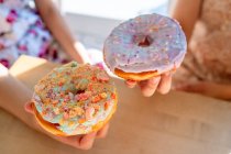 Cropped female hands carrying round glazed pastries with sprinkles while sitting by table — Stock Photo