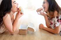 Happy women with box of glazed desserts sitting at table — Stock Photo