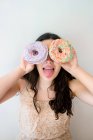 Carefree woman having fun and playing with glazed pastries with sprinkles while standing by white wall — Stock Photo