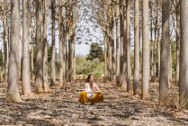 Спокойная беременная женщина, практикующая йогу, сидя в позе лотоса на земле в парке — стоковое фото
