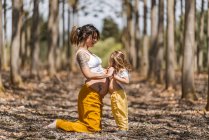 Вид збоку весела босоніж вагітна жінка і маленька дівчинка тримає руки в осінньому лісі галявина — стокове фото