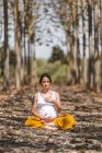 Calm adult pregnant woman practicing yoga while sitting in pose lotus on ground in park — Stock Photo