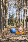Взрослая безмятежная женщина медитирует на большом синем мяче, сидя на земле среди деревьев в парке — стоковое фото