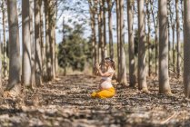 Спокійна доросла вагітна жінка практикує йогу, сидячи в позі лотос на землі в парку — стокове фото