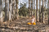 Спокійний дорослий вагітна жінка медитує, сидячи в позі лотос на землі в парку — стокове фото