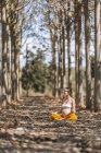 Femme enceinte adulte calme méditant tout en étant assis dans la pose lotus sur le sol dans le parc — Photo de stock