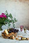 Uvas ao lado de pedaço de queijo em tábuas de corte perto de flores rosa — Fotografia de Stock