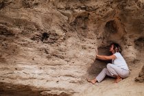 Side view of woman sitting in cavern in rough stone cliff and meditating while practicing Tai Chi in countryside — Stock Photo