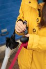 Неузнаваемая женщина в жёлтой куртке открывает мешок с собачьими какашками, держа поводок на улице. — стоковое фото