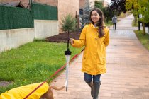 Woman in yellow jacket walking with English Pointer dog in yellow cloak on leash in rainy weather in street — Stock Photo