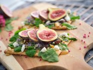 Homemade open sandwiches with slices of fig and cheese on rye bread with rocket salad on wooden board — Stock Photo
