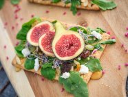 Homemade open sandwich with slices of fig and cheese on rye bread with rocket salad on wooden cutting board — Stock Photo