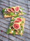 Homemade open sandwiches with slices of fig and cheese on rye bread with rocket salad on gray surface — Stock Photo