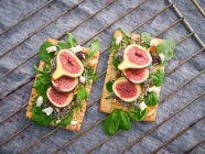 Homemade open sandwiches with slices of fig and cheese on rye bread with rocket salad on gray surface — Stock Photo