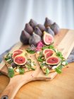 Sanduíches caseiros abertos com fatias de figo e queijo no pão de centeio com salada de foguete na placa de corte de madeira — Fotografia de Stock