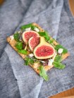 Homemade open sandwich with slices of fig and cheese on rye bread with rocket salad on grey towel — Stock Photo