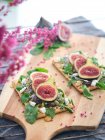 Homemade open sandwiches with slices of fig and cheese on rye bread with rocket salad on wooden cutting board — Stock Photo