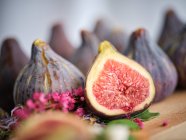 Ripe whole and sliced figs among flavored green leaves of herbs and colorful flowers on wooden cutting board — Stock Photo