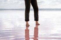 Low section of barefoot man in black pants standing in still sea by shore on cloudy weather — Stock Photo