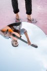 Von oben Spiegelung des Mannes, der Gitarre spielt, während er im Wasser an der Küste über dem blauen Himmel im ovalen Spiegel steht — Stockfoto