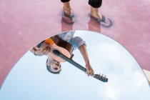 Зверху відбиття людини, що грає на гітарі, стоячи у воді над блакитним небом в овальному дзеркалі — стокове фото