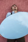 Зверху виснажливий чоловік лежить на рожевій воді, тримаючи овальне дзеркало, що відображає блакитне небо — стокове фото