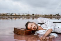 Sleepy man lying down with closed eyes with acoustic guitar in sea at sandbank — Stock Photo