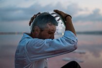Homme pensif en chemise mouillée sortant aquarium vide tout en restant assis au bord de la mer au crépuscule — Photo de stock
