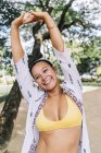 Donna allegra in bikini sorridente e in piedi con le mani in alto, guardando lontano sulla strada in Costa Rica — Foto stock