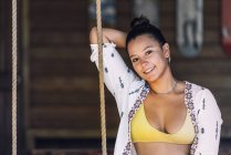Abbronzata donna felice in abbigliamento casual seduto su altalene e guardando la fotocamera sopra parete di legno in Costa Rica — Foto stock