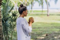 Side view peaceful woman drinking coffee from mug and standing by palm tree on sunny seaside in Costa Rica — Stock Photo