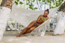 Erfreut Frau im Badeanzug sitzt mit Handy in Hängematte an exotischer Küste in Costa Rica — Stockfoto