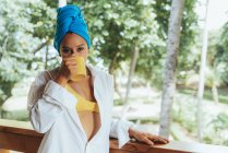 Content woman in head wrap enjoying hot drink while standing by wooden railing and gazing at leafy trees in Costa Rica — Stock Photo