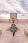 Задній вигляд жінки в декоративному пальто стоїть на старовинній площі проти хмарного неба в Бухарі (Узбекистан). — стокове фото