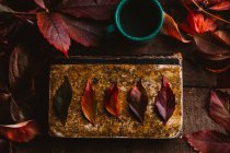 Dall'alto libro d'epoca invecchiato con foglie di autunno giallo arancio rosso brillante e coppa verde con bevanda sul tavolo di legno — Foto stock