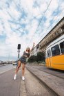 Aktive schlanke Frau hebt die Hand als wartende Straßenbahn in der Nähe der Bahn in hell bewölkten Tag in Budapest — Stockfoto