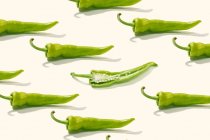 Dall'alto composizione creativa di pepe verde a fette con semi tra peperoni interi su superficie bianca — Foto stock