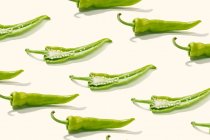 Dall'alto composizione creativa di pepe verde a fette con semi tra peperoni interi su superficie bianca — Foto stock
