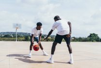 Vista laterale di ragazzi afroamericani che giocano a basket nella giornata luminosa sul campo da gioco — Foto stock