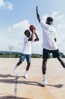 Vista lateral de chicos afroamericanos jugando baloncesto en día brillante en el patio de recreo - foto de stock