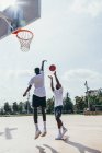 Vue latérale de gars afro-américains jouant au basket dans la journée brillante sur le terrain de jeu — Photo de stock
