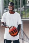Allegro giocatore afroamericano che tiene la palla arancione e guarda la fotocamera con la lingua fuori con ampio sorriso — Foto stock