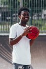 Allegro giocatore afroamericano che tiene la palla arancione e distoglie lo sguardo con ampio sorriso — Foto stock