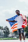 Sérieux homme afro-américain tenant le drapeau américain sur l'épaule et détournant les yeux — Photo de stock
