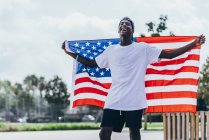 Серйозний афроамериканець тримає американський прапор на плечі і озирається — стокове фото